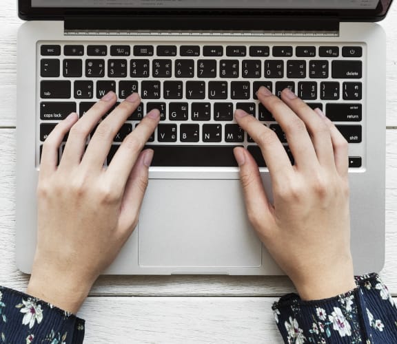 View of a womans hands on a laptop with a cup of tea sitting next to it
