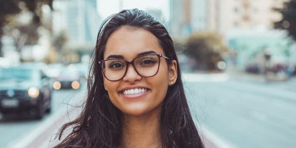 Woman with glasses standing in the street smiling at the camera with her nice white teeth